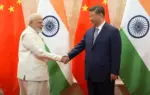 ভারতের প্রধানমন্ত্রী নরেন্দ্র মোদি এবং চীনের প্রেসিডেন্ট শি জিনপিং হাত মেল্লাচ্ছেন এবং পিছনে দুই দেশের পতাকা দেখা যাচ্ছে।