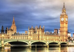 যুক্তরাজ্যের সংসদ ভবন এবং ওয়েস্টমিনস্টার সেতু রাতের আলোয় দেখা যাচ্ছে। ভবনটির ঐতিহাসিক স্থাপত্য অন্ধকার আকাশে উজ্জ্বলভাবে আলোকিত, যা লন্ডনের বিখ্যাত ল্যান্ডমার্ককে ফুটিয়ে তুলেছে।