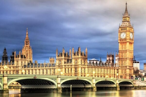 যুক্তরাজ্যের সংসদ ভবন এবং ওয়েস্টমিনস্টার সেতু রাতের আলোয় দেখা যাচ্ছে। ভবনটির ঐতিহাসিক স্থাপত্য অন্ধকার আকাশে উজ্জ্বলভাবে আলোকিত, যা লন্ডনের বিখ্যাত ল্যান্ডমার্ককে ফুটিয়ে তুলেছে।