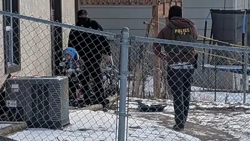 মুখোশ পরিহিত ইমিগ্রেশন পুলিশের সদস্যরা শিশুটির পাশে দাঁড়িয়ে আছেন।